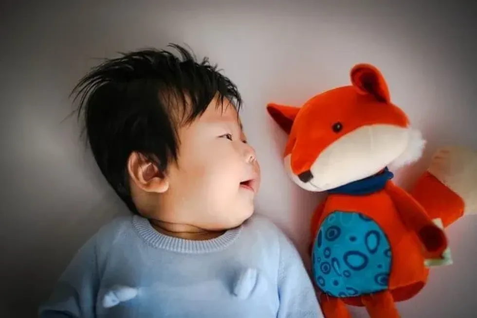 A baby boy laying on bed next to his fox toy