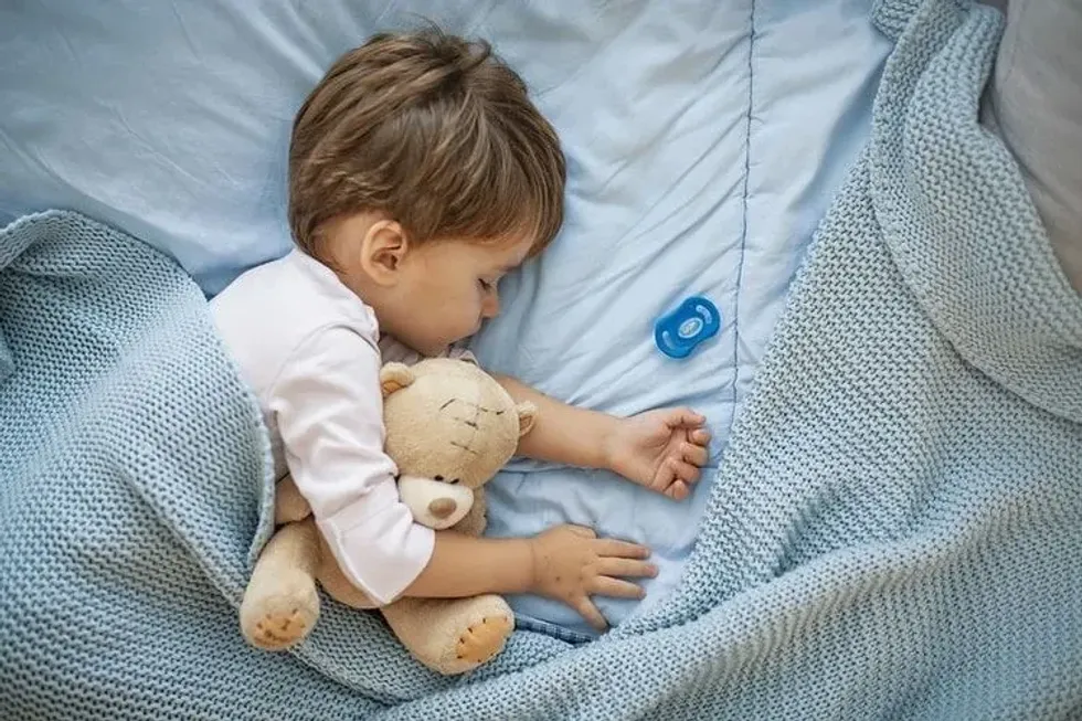 A baby boy sleeping with his teddy bear