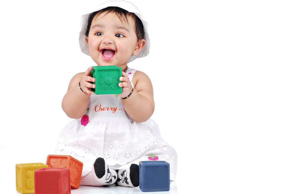 A baby girl wearing a sun hat, playing with colorful blocks.