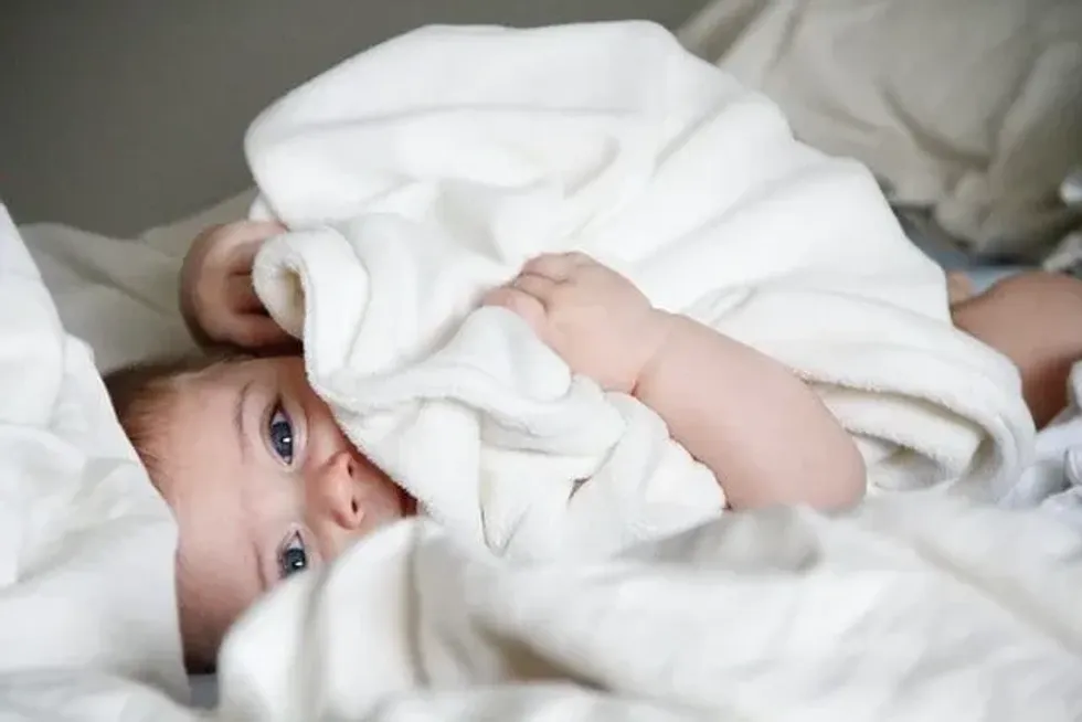 A baby lying in bed with white blanket