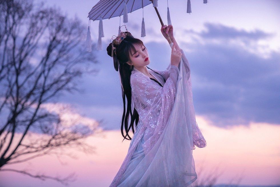 A beautiful Japanese girl swathed in a lavender-colored Japanese attire, holding up an umbrella