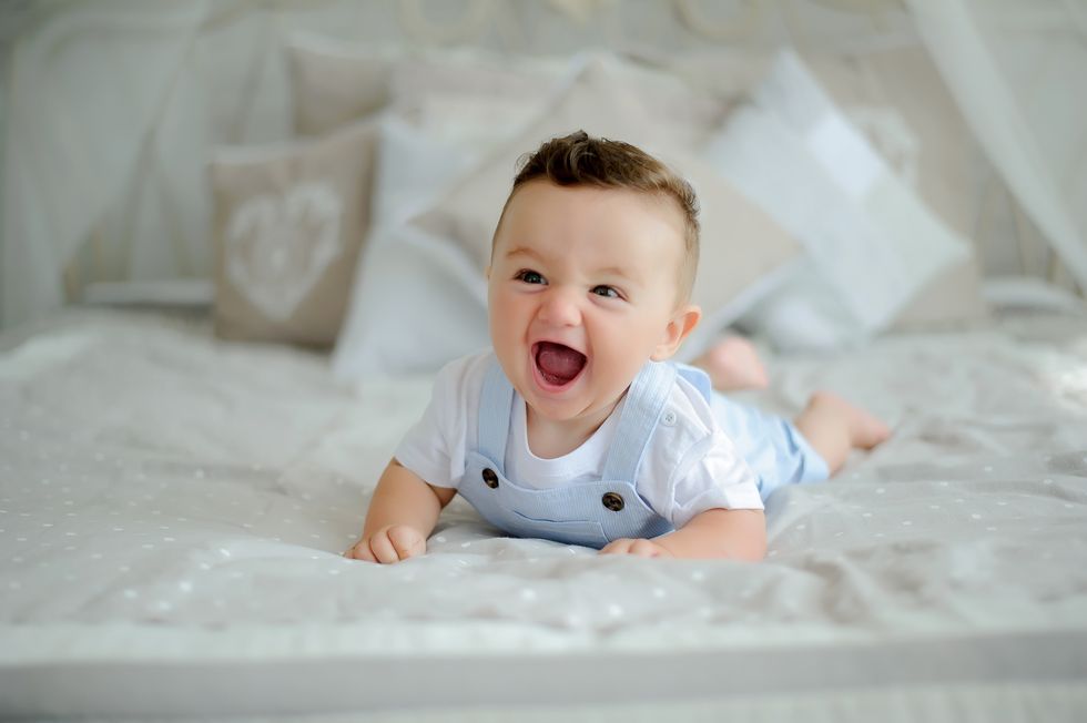 A delighted baby boy with a wide smile, lying on a bed.