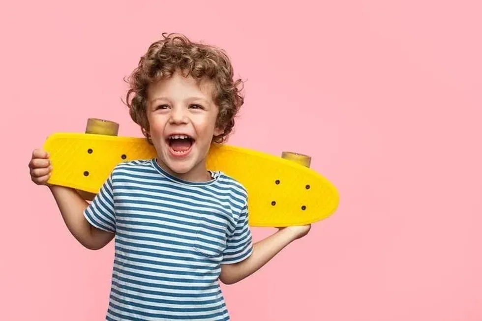 A happy boy holding a yellow skateboard behind his back