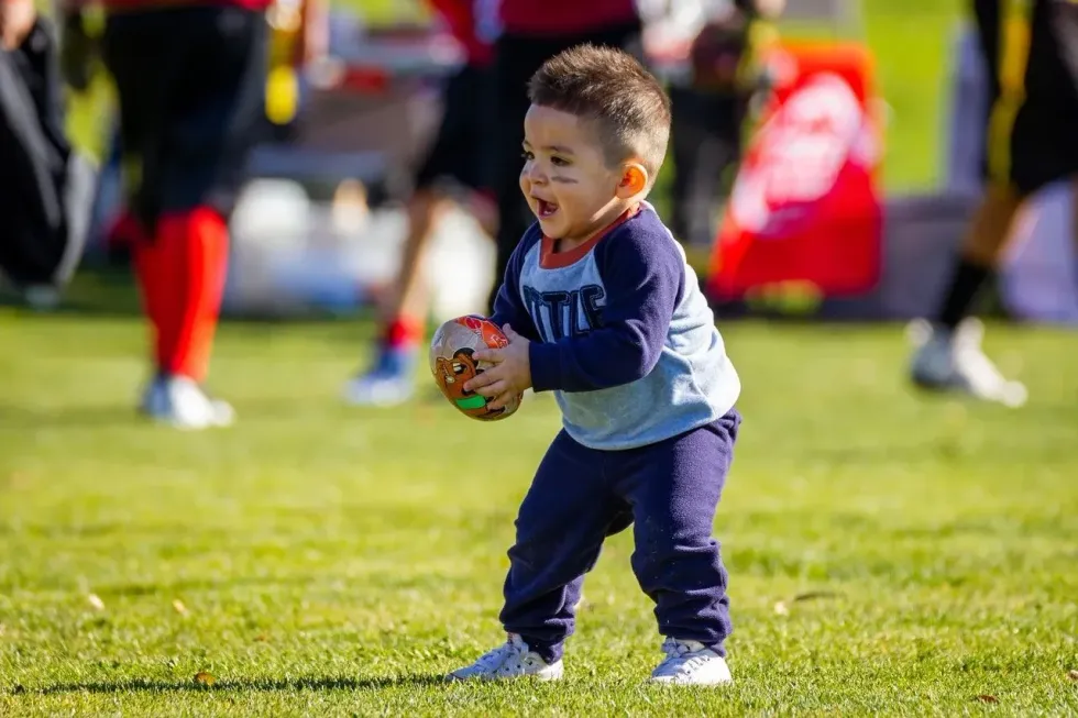 A little boy holding football on ground