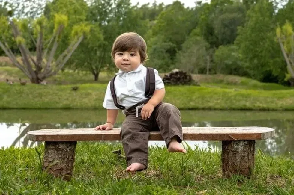 A little boy sitting on a bench in a park