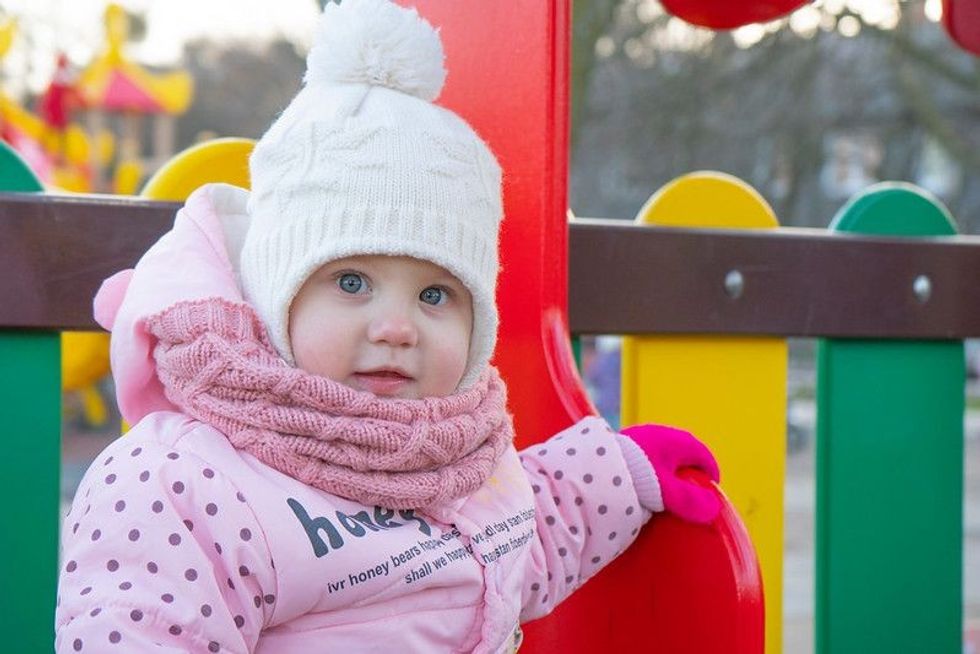 A little girl in a pink jacket close up sitting on the Playground 3