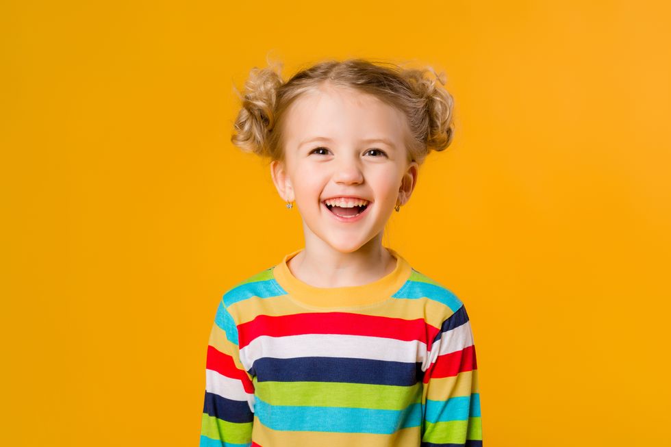 A little girl wearing a multicolored sweater and smiling.