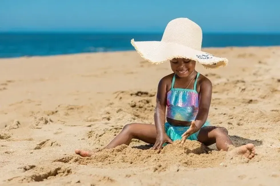 A little girl wearing mermaid dress is playing in sand on a beach