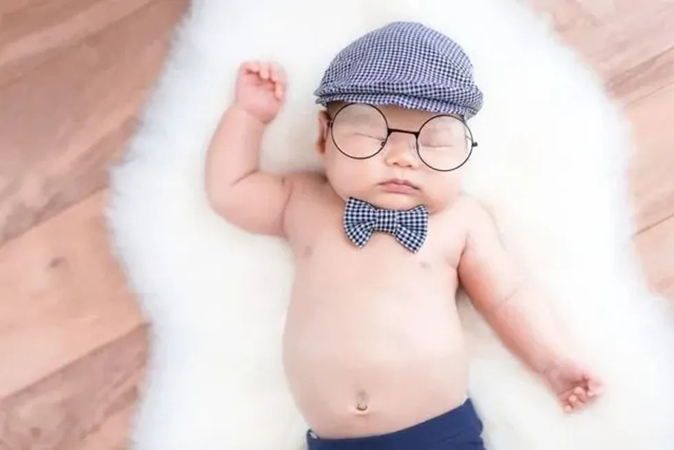 A newborn baby boy wearing cap and bow is sleeping on white fur