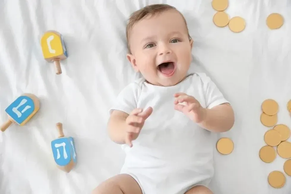 A newborn baby lying near dreidels and chocolate coins on bed.