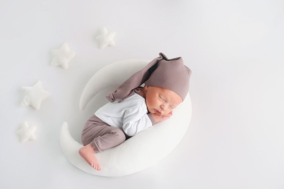 A serene posh baby boy sleeps on a crescent moon pillow among plush stars, embodying a celestial nursery theme.