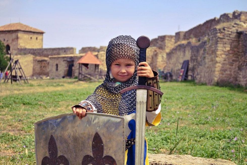 A small but very brave girl in armour and chain mail with sword and shield in a medieval castle.