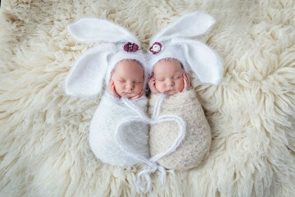 Adorable newborn baby twin girls wearing bunny hats sleeping on the fur.