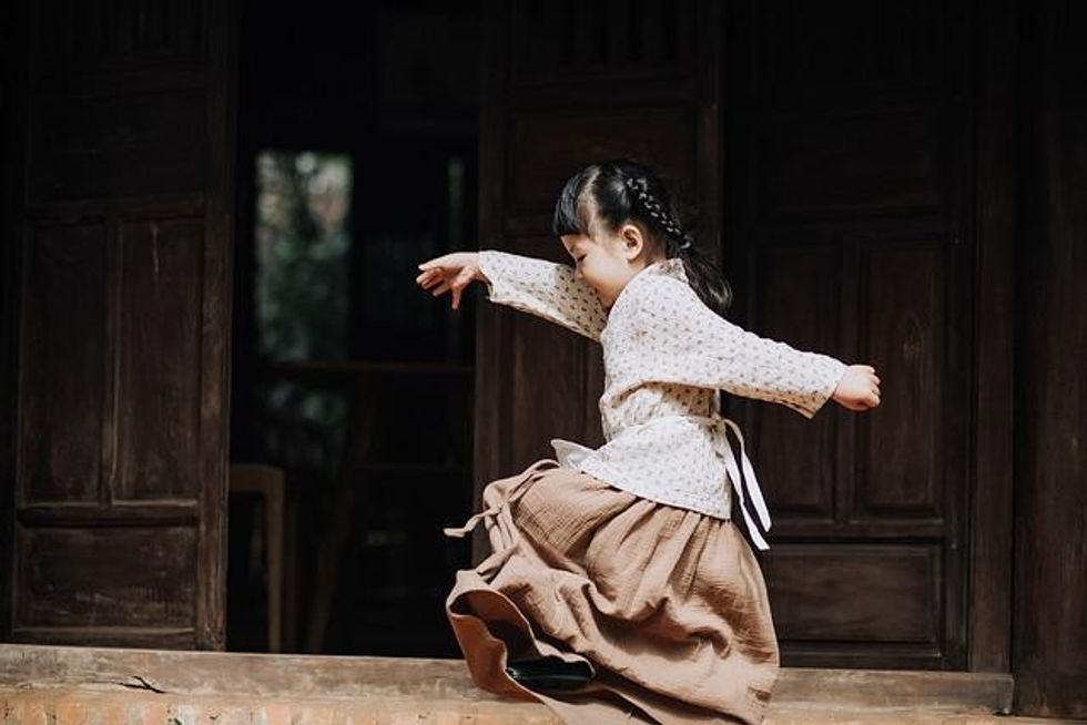 An adorable little Japanese girl with arms outstretched happily in a playful stance