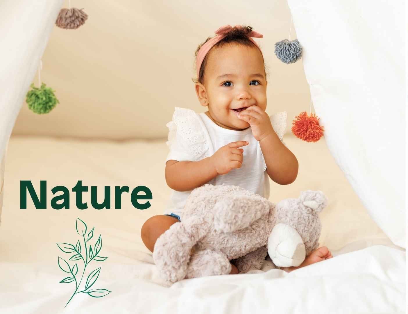 An image of a cute baby sitting in her crib, hand in her mouth with a doll on her leg with the inscription Nature.