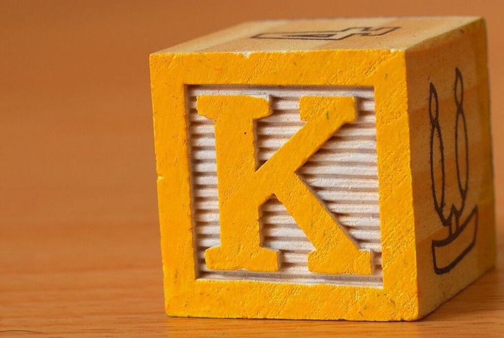 An image of a yellow wooden cube dice showing the letter K