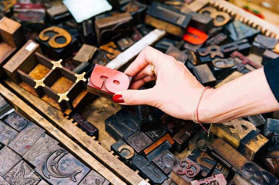 An image showing in alphabets crested on a metal tiles in a chest box and a lady's hand with red polished nails holding the alphabet e