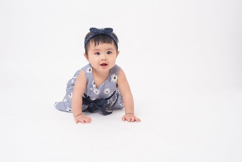 Asian baby girl wearing blue bow and floral dress crawling