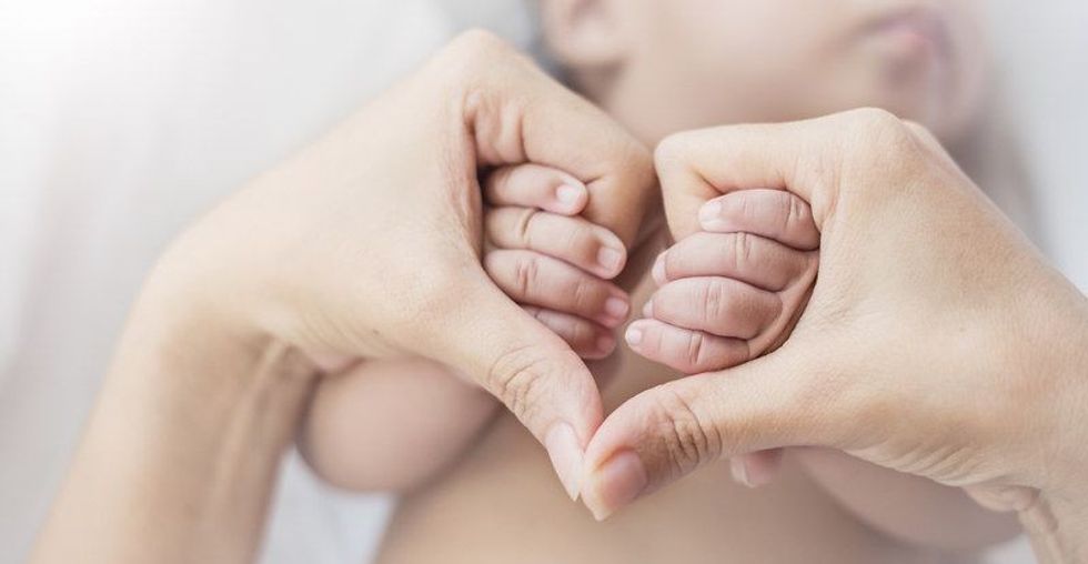 Asian newborn baby holding mother hands in heart shape