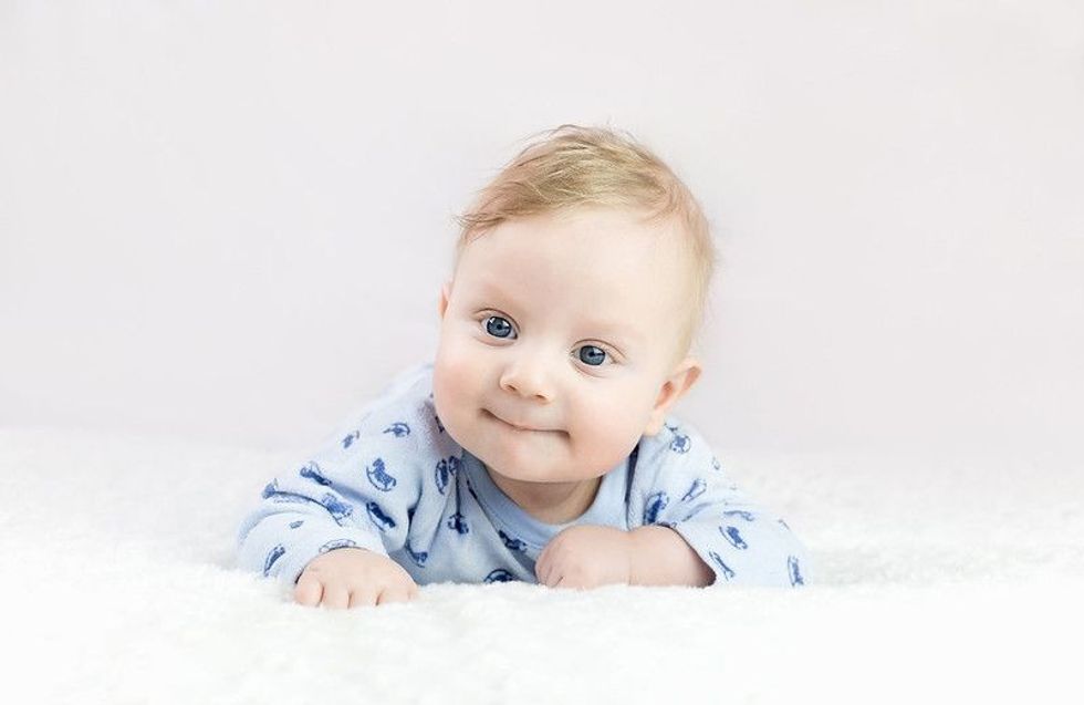 Baby boy lying on bed in blue dress.