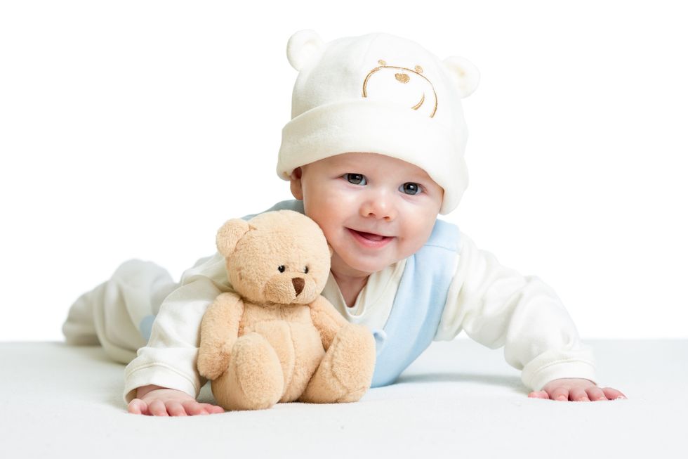 Baby boy lying on his chest and playing with a teddy bear. 