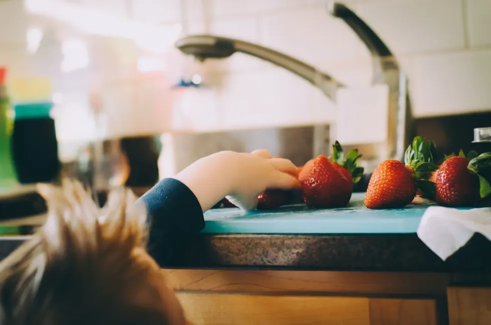 Baby boy trying to steal strawberries from kitchen