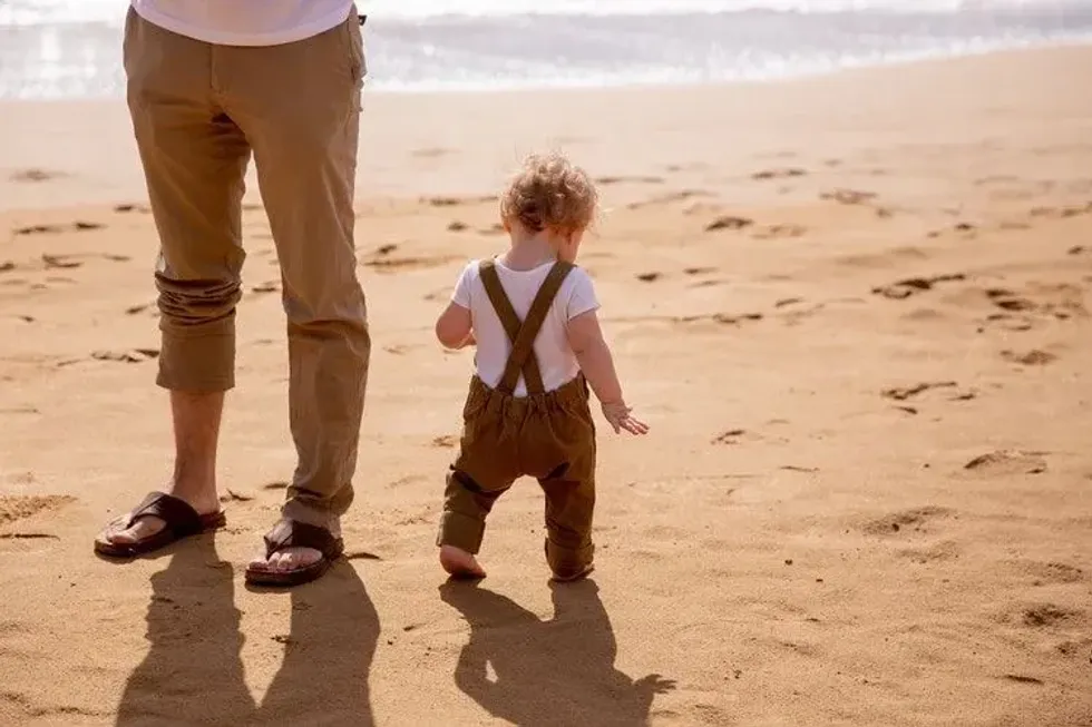 Baby boy walking with his father on the beach