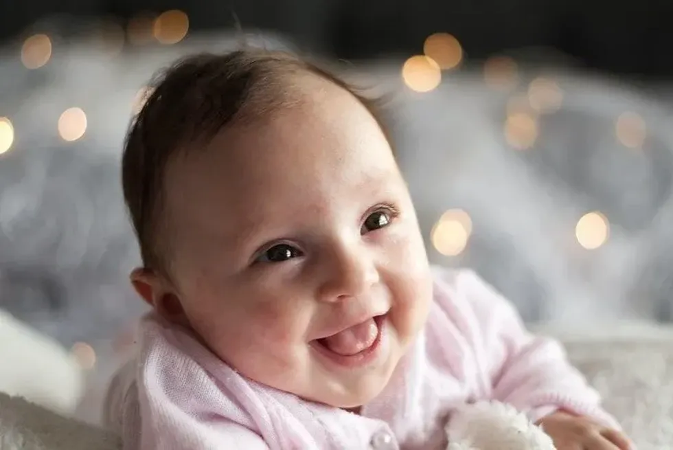 Baby girl in pink smiling and looking up at her parents.