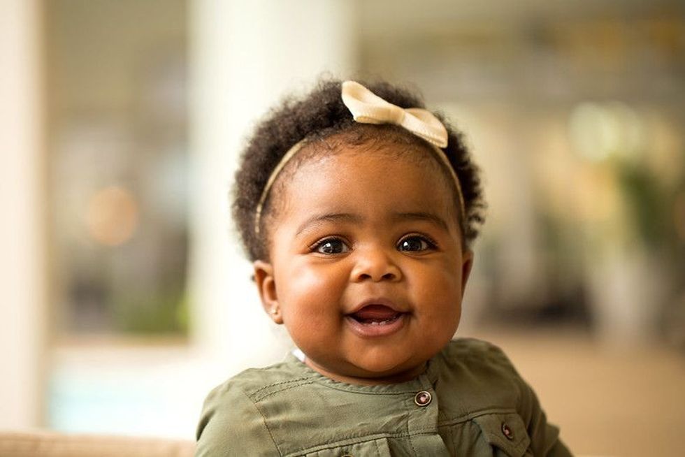 Baby girl wearing a yellow bow smiling.