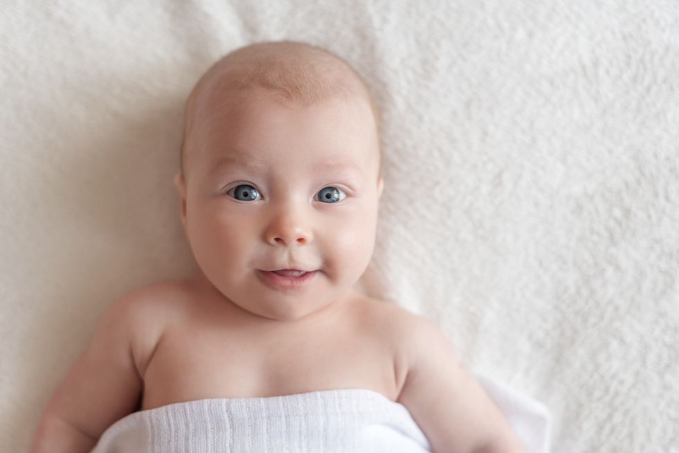 Baby girl with blue eyes smiling on a white blanket.