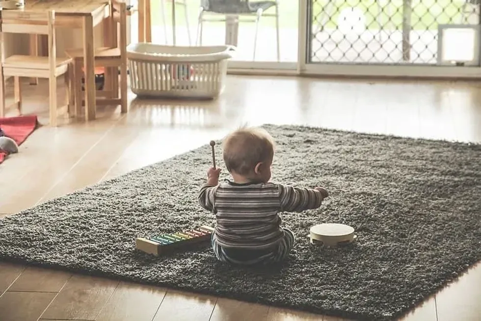 Baby sitting on a rug on the floor playing with toy musical instruments.