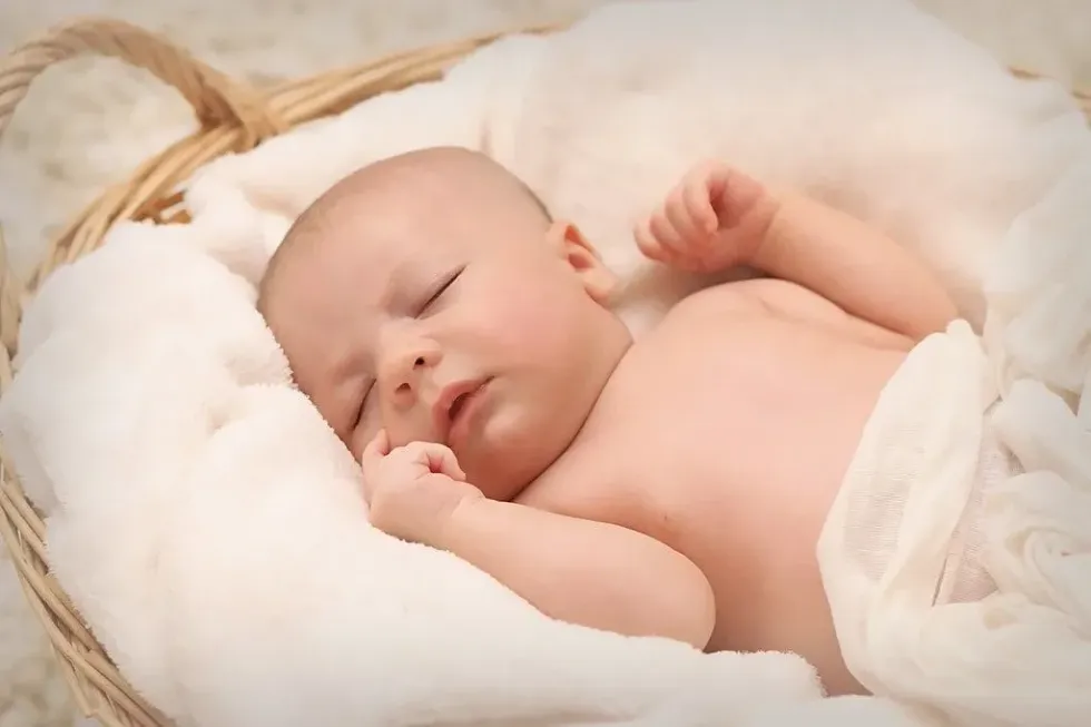 Baby sleeping peacefully in white sheets and blankets in a Moses basket.