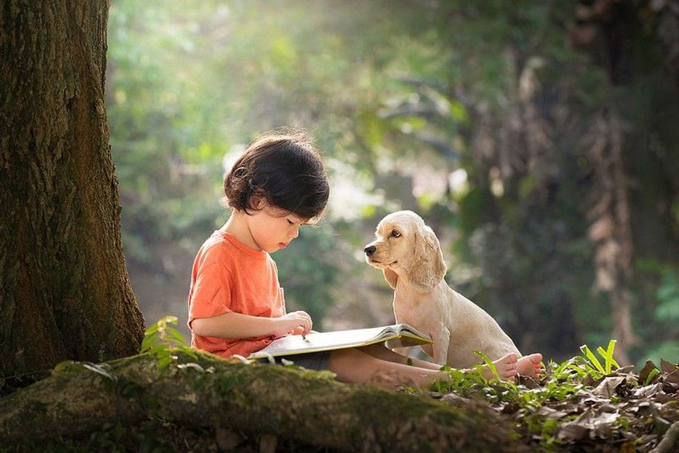 Child and puppy sitting under tree