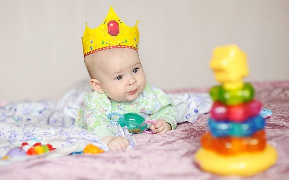 Child in the crown lies on a bed with toys