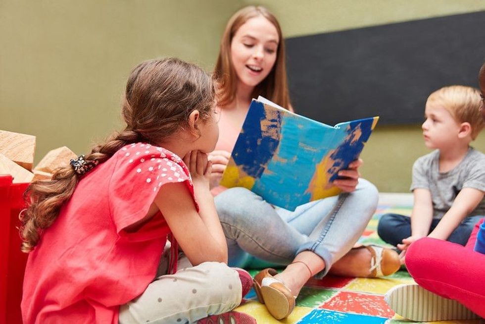 Childminder and children reading from a children's book in a kindergarten