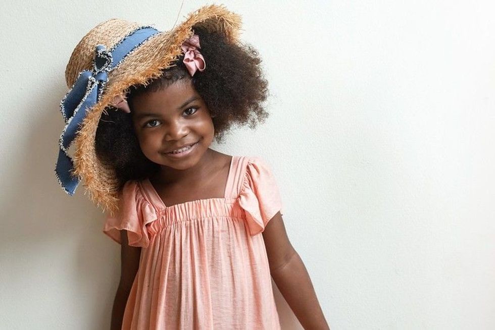 Cute afro little girl wearing straw hat and old rose color dress