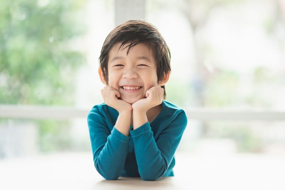 Cute Asian child resting chins on hands on wooden table