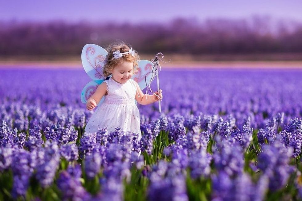 Cute curly little girl in flower crown and fairy costume with wings and magic wand