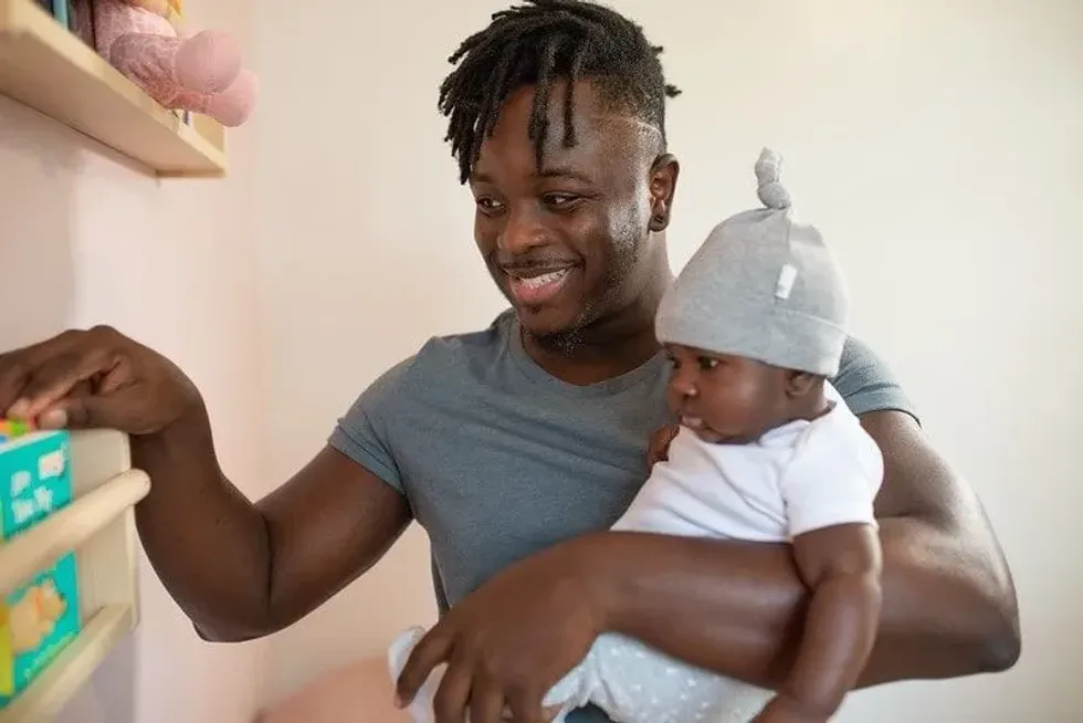 Dad holding his baby son in his arm showing him the bookshelf.