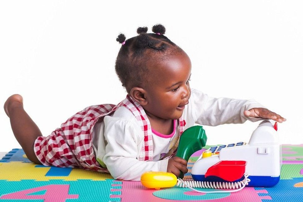 Ethnic baby girl playing with toy telephone