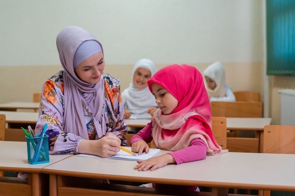 Female hijab Muslim teacher helps student girl to finish the lesson