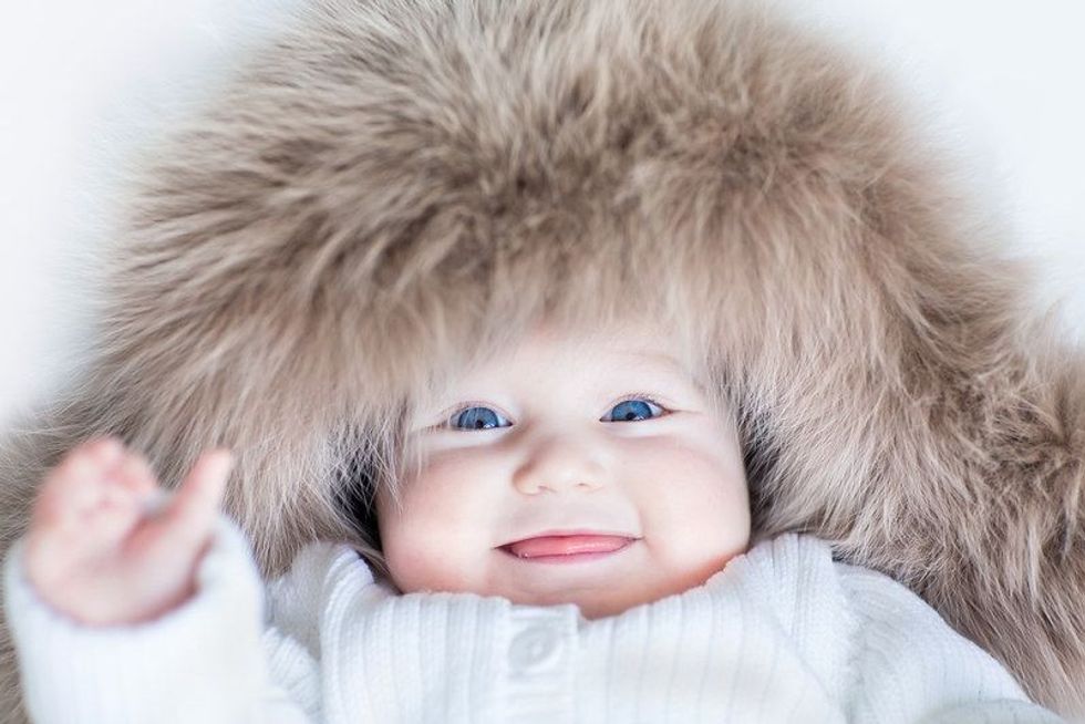 Funny cute baby girl with big blue eyes wearing a huge winter hat and a warm knitted jacket.