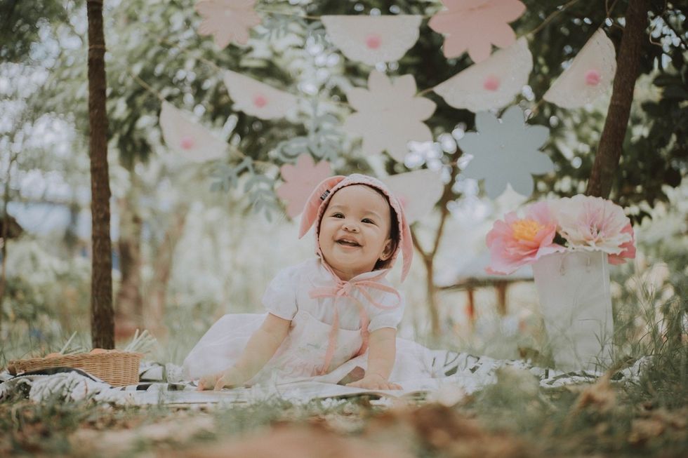 Happy baby girl in forest with flowers and flowery bunting above her head