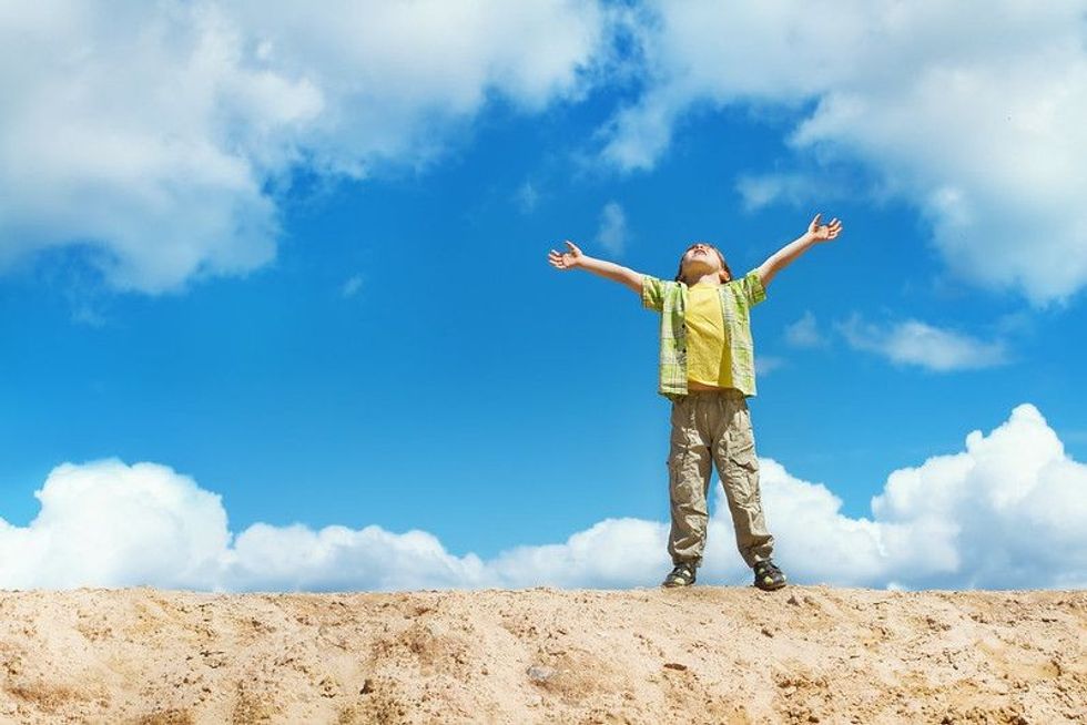 Happy child standing on the top with hands raised up representing look up at the sky day.