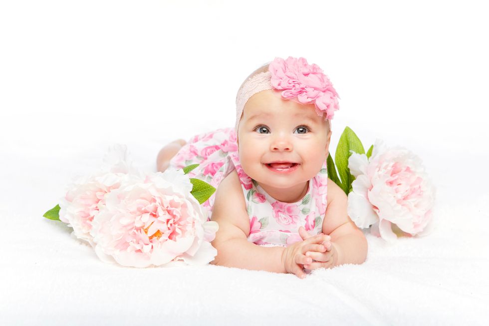 Happy little baby girl surrounded by big pink pastel flowers