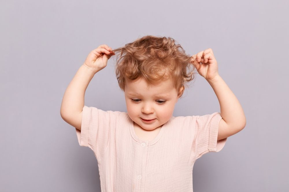 Indoor shot of beautiful adorable happy cute charming baby infant girl pulling her wavy blond hair