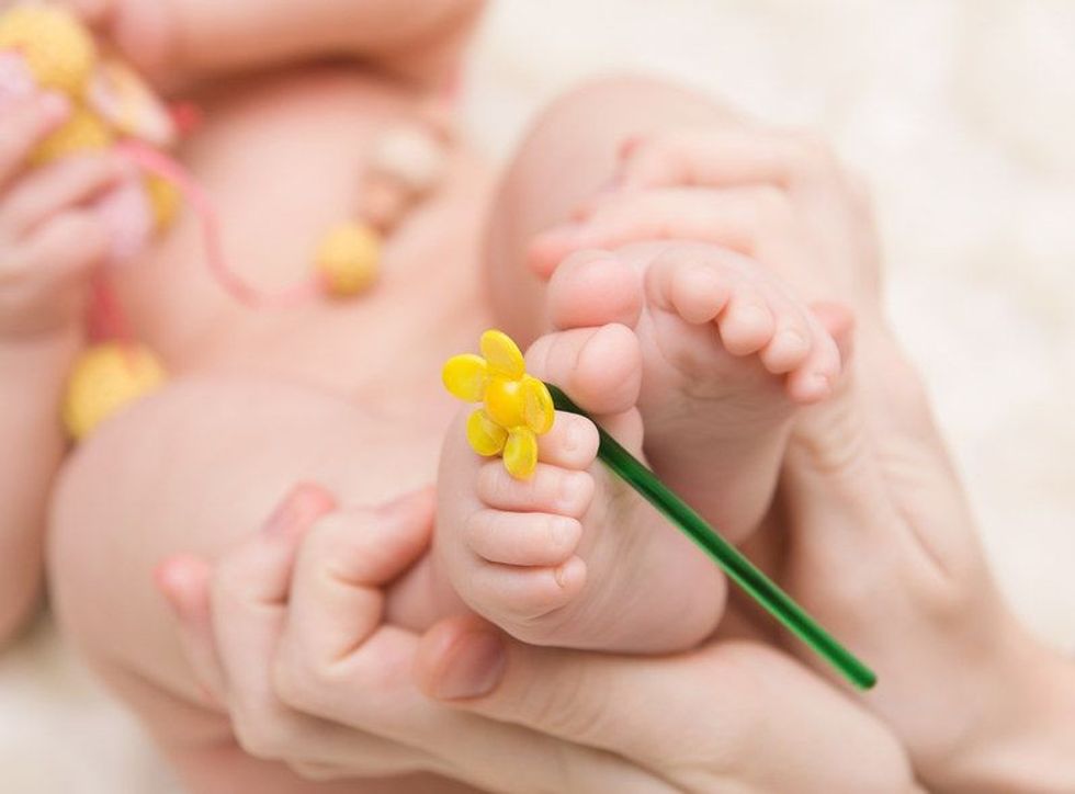 Little baby feet with yellow flower in the mother's hands.