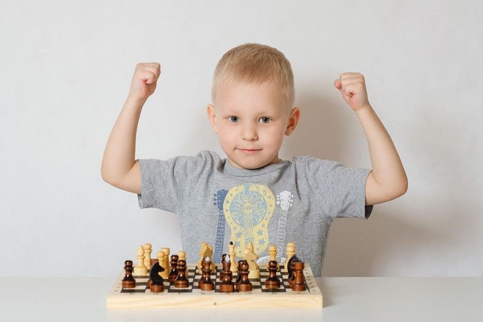 Little blond boy sitting at the table and playing chess