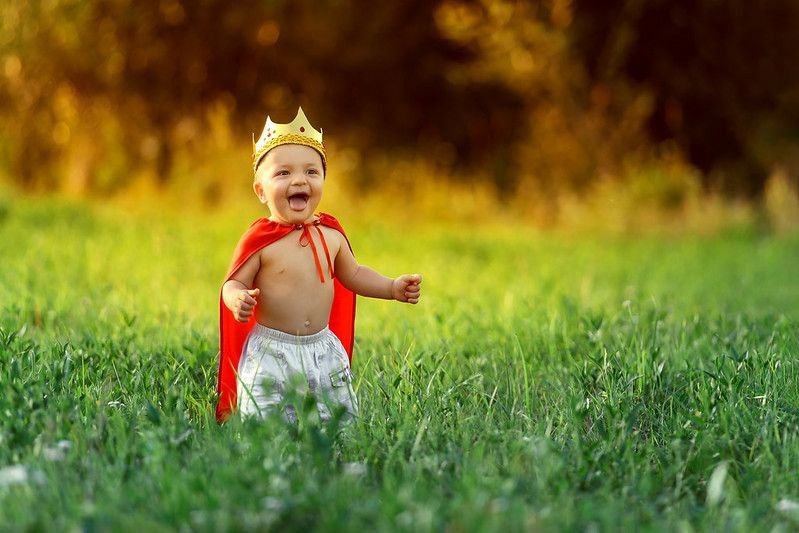 Little boy prince,child king laughing summer day outdoors around colorful green grass.