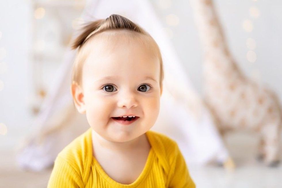 Little cute baby girl is sitting in a bright cozy children's playroom.